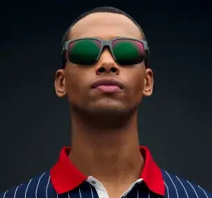 Un uomo mulatto di circa 35 anni, indossa una polo a righe blu e bianche con colletto rosso e occhiali da sole. Gli occhiali hanno una montatura quadrata in plastica resistente di colore verde khaki opaco, lenti resistenti all'acqua di colore fumo con riflessi verdi.