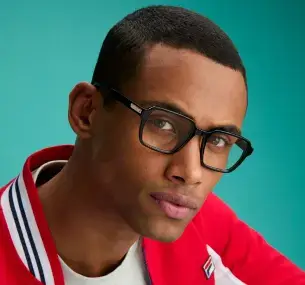 Un uomo mulatto di 35 anni, con capelli neri corti, indossa una felpa rossa e bianca e occhiali da vista in acetato nero con un dettaglio in metallo sull'asta che riporta il logo FILA inciso con la lettera F.