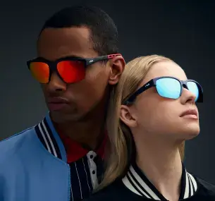 Un uomo mulatto di circa 35 anni e una donna con pelle chiara e capelli biondi, entrambi con occhiali da sole della linea Performance. Gli occhiali, dal design leggero e ispirato al mondo delle corse, hanno lenti con riflessi rossi per l'uomo e riflessi blu per la donna.
