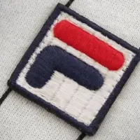 Due atleti stanno giocando a tennis su un campo all’aperto con uno sfondo di cielo nuvoloso. Entrambi indossano completi sportivi coordinati, composti da magliette gialle, pantaloncini neri e scarpe da tennis. Uno dei giocatori è in volo, intento a colpire la palla con una racchetta, mentre l’altro è in posizione difensiva, pronto a rispondere. L’immagine trasmette azione, competizione e dinamismo.